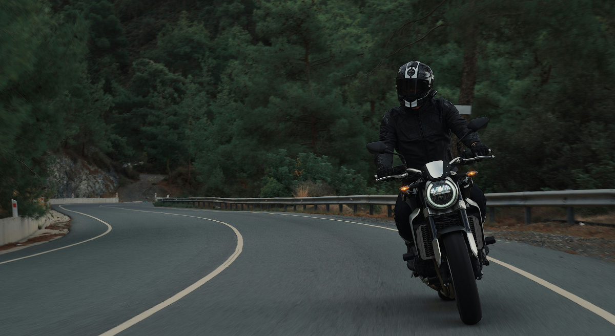 Motorcyclist riding on a winding country road with forest in the background.